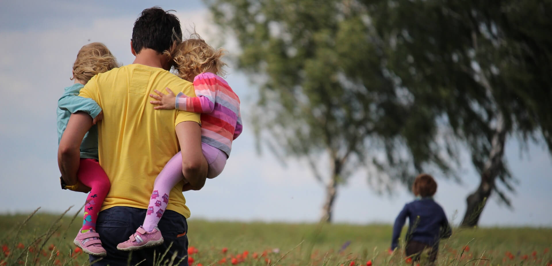 Père avec deux enfants dans les bras marchant dans un champ
