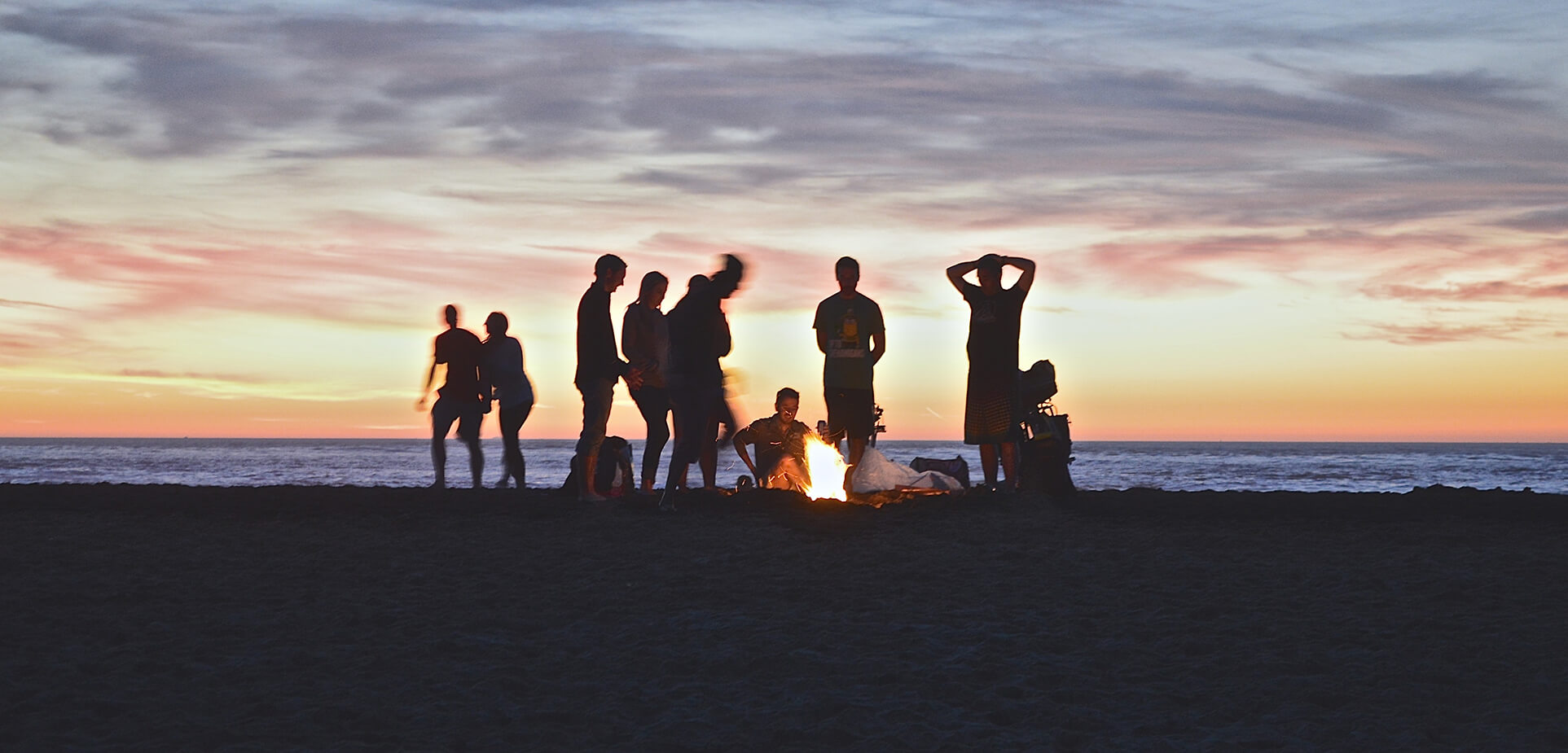 Famille autour d'un feu sur une plage lors d'un couchers de soleil